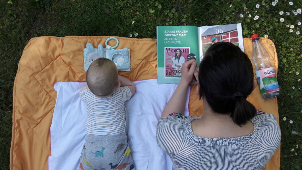 Mutter und Sohn liegen auf dem Bauch auf einer Decke im Park und lesen