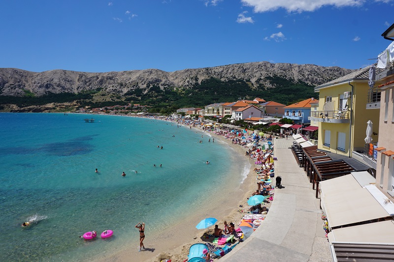 Der Strand von Baska auf der Insel Krk im Hochsommer mit vielen Gästen und Sonnenschirmen