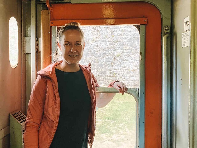 Stefanie steht am Fenster eines Nachtzugs und blickt freundlich in die Kamera